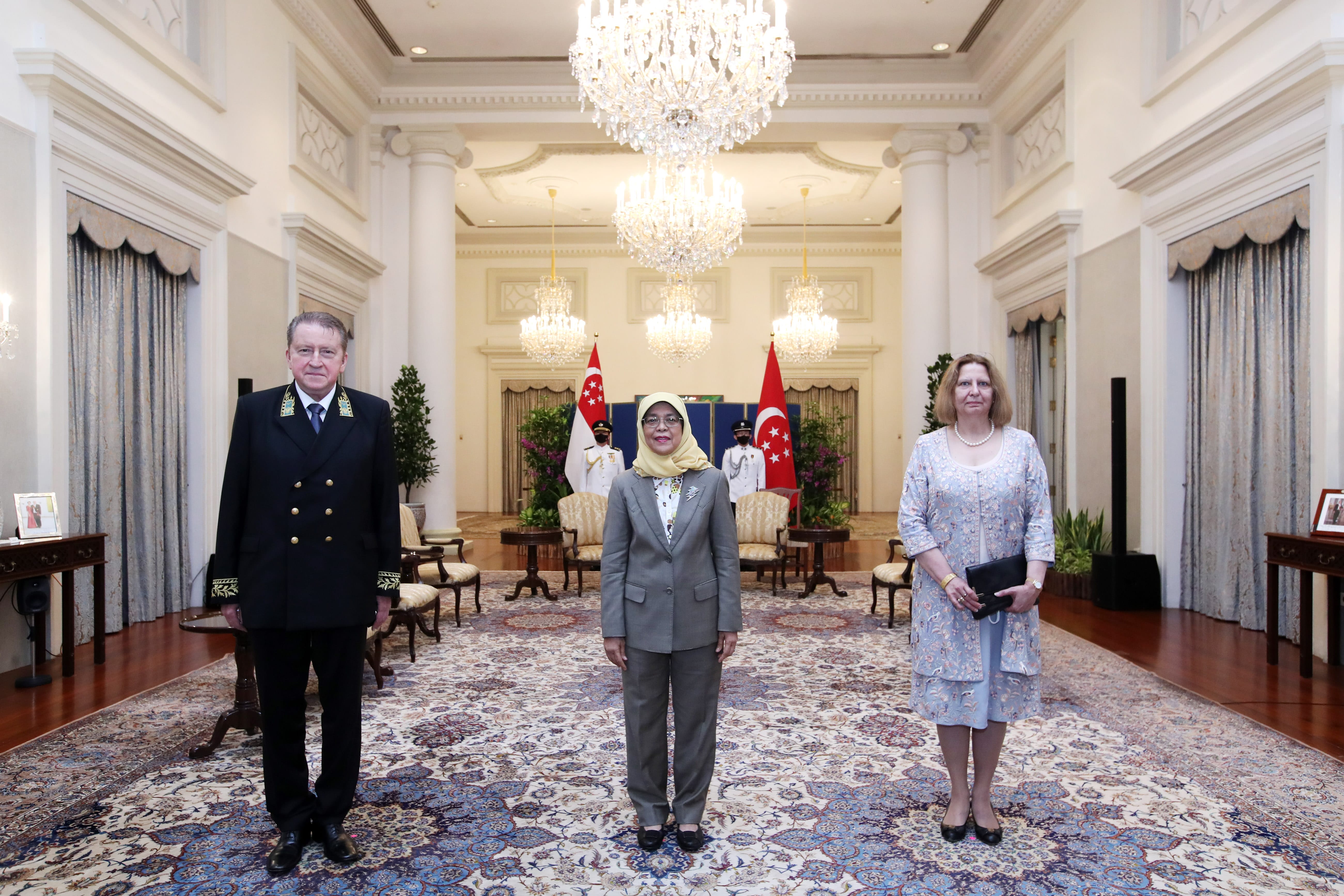 Singapore's President Halimah Yacob stands between two people in ornate room.